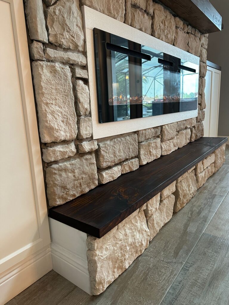 Stone fireplace wall with floating wood bench and mounted TV in modern Florida home