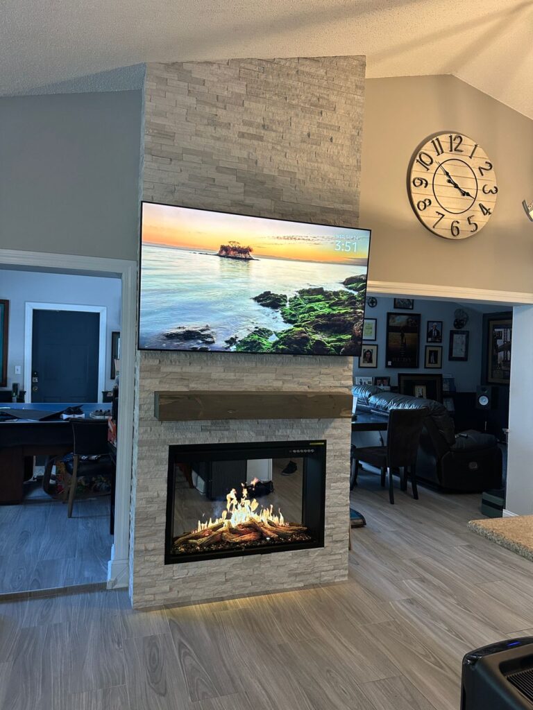 Floor-to-ceiling stone fireplace column with mounted TV, modern electric fireplace, and contemporary vertical fireplace wall design.