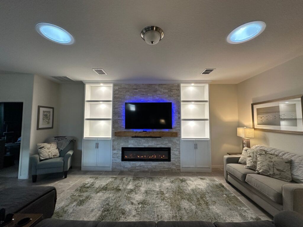 Classic stone fireplace wall with recessed TV, wood mantel, built-in shelving, LED lighting, cabinets, and linear fireplace