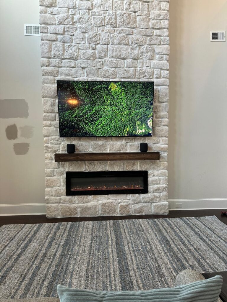 Front view of floor to ceiling stone fireplace with mounted TV, floating mantel, and linear electric fireplace