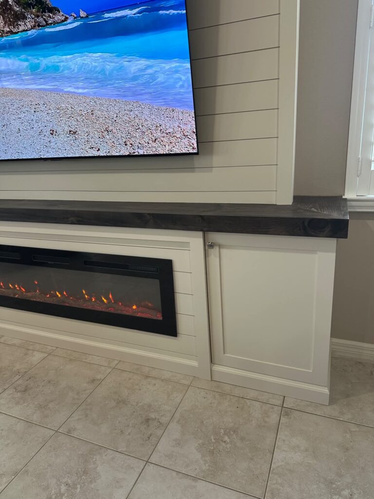 Linear electric fireplace built into white shiplap fireplace wall with lower storage