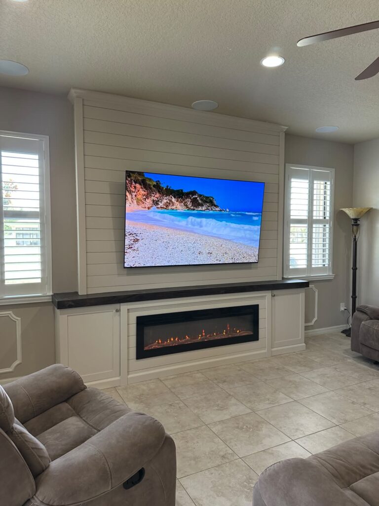 White shiplap fireplace wall with built in base, dark countertop, TV layout, crown molding, trim details, and electric fireplace
