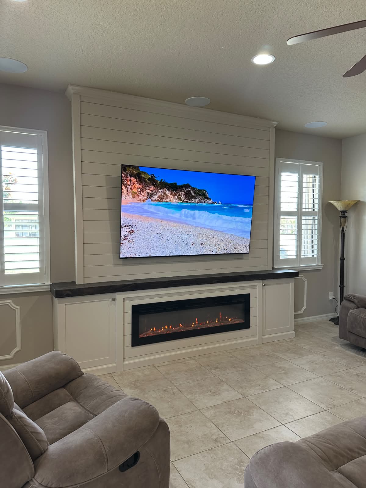 White shiplap fireplace wall with built in base, dark countertop, TV layout, crown molding, trim details, and electric fireplace
