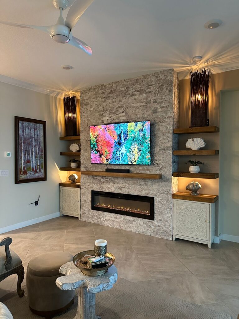 Stone fireplace TV wall with floating shelves, natural stone texture, ambient lighting, wood mantel, and linear fireplace