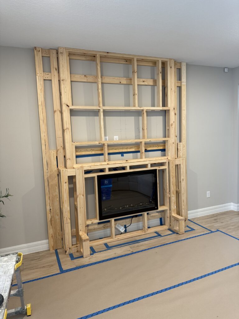 White brick fireplace wall construction with custom multi-level framing for TV and electric fireplace