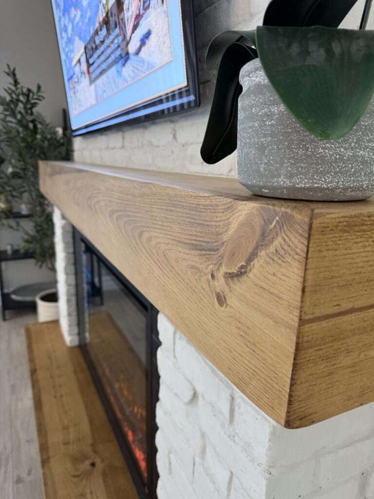 Handcrafted wood mantel detail on white brick fireplace wall with electric fireplace below