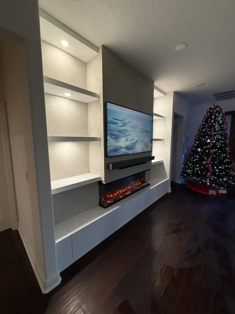 Limewash fireplace TV wall built into existing niche with illuminated shelves, hidden storage, and 3D fireplace