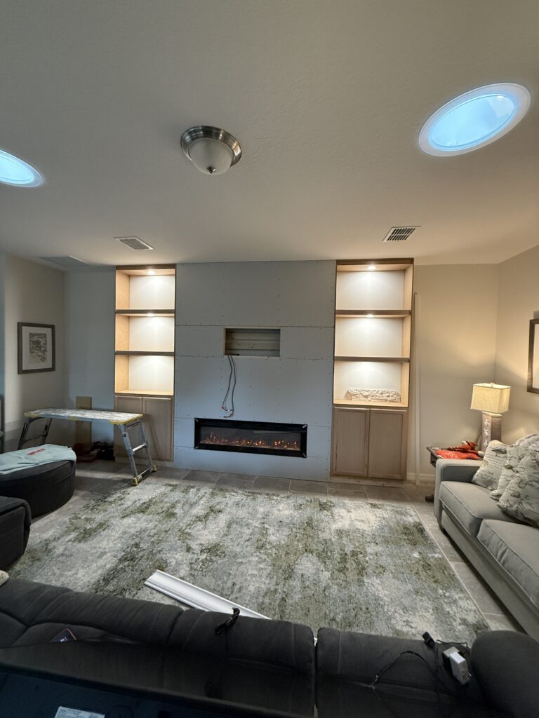 Classic stone fireplace wall during drywall stage with built-in shelving, LED lighting, and fireplace installation