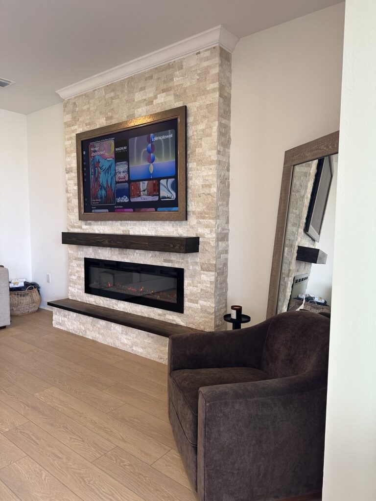 Custom stone fireplace media wall featuring ledger stone, recessed TV placement, floating wood mantel, matching bench, and modern linear electric fireplace.
