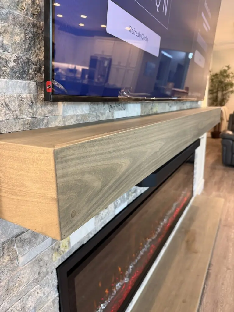 Floating wood mantel detail on stone fireplace media wall with recessed TV and electric fireplace