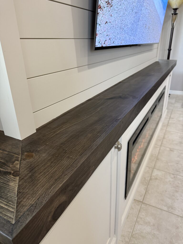 White shiplap fireplace wall with TV above linear electric fireplace and dark countertop