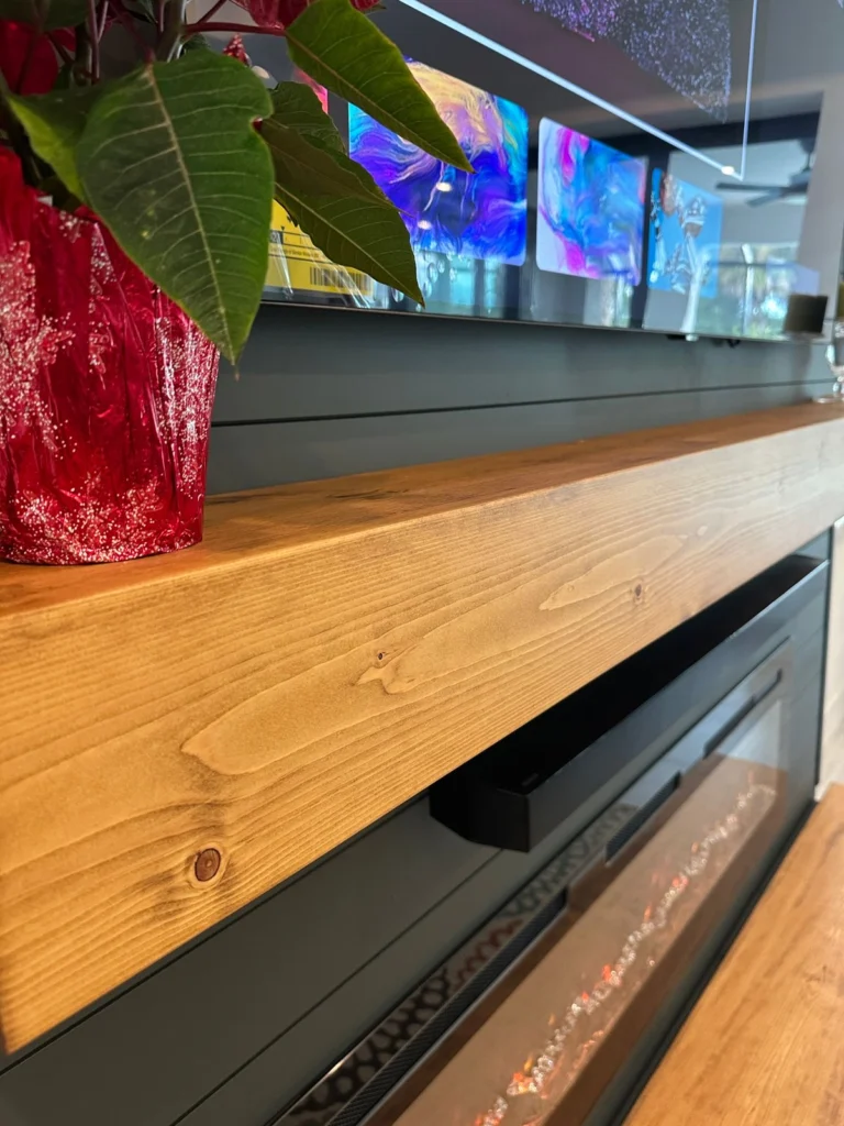 Close-up of the stained wood floating mantel on a dark shiplap fireplace wall