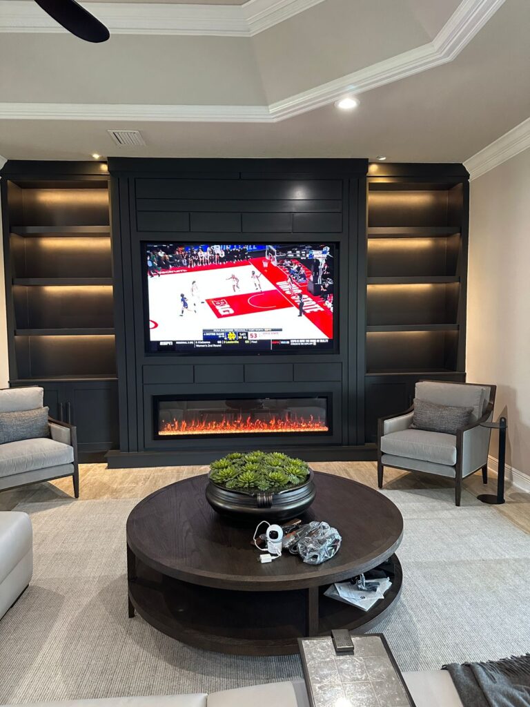 Finished dark built in media wall with recessed TV, LED lighting, cabinets, and linear fireplace