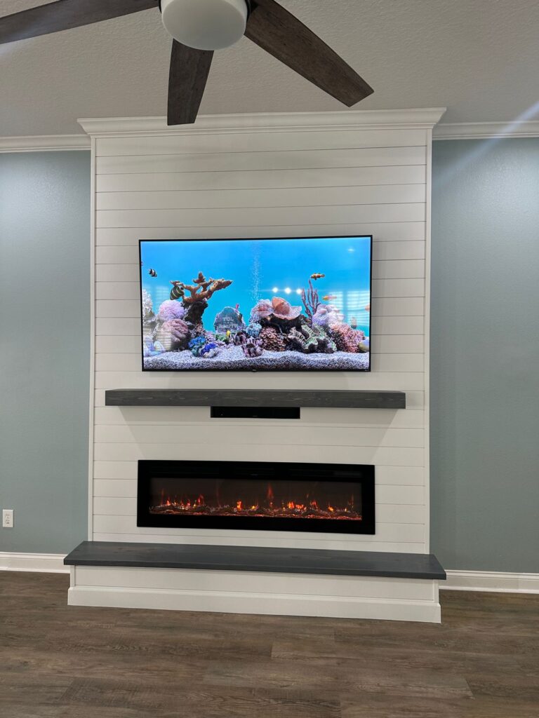 Custom white shiplap fireplace wall featuring a floating wood mantel, TV integration, and modern electric fireplace