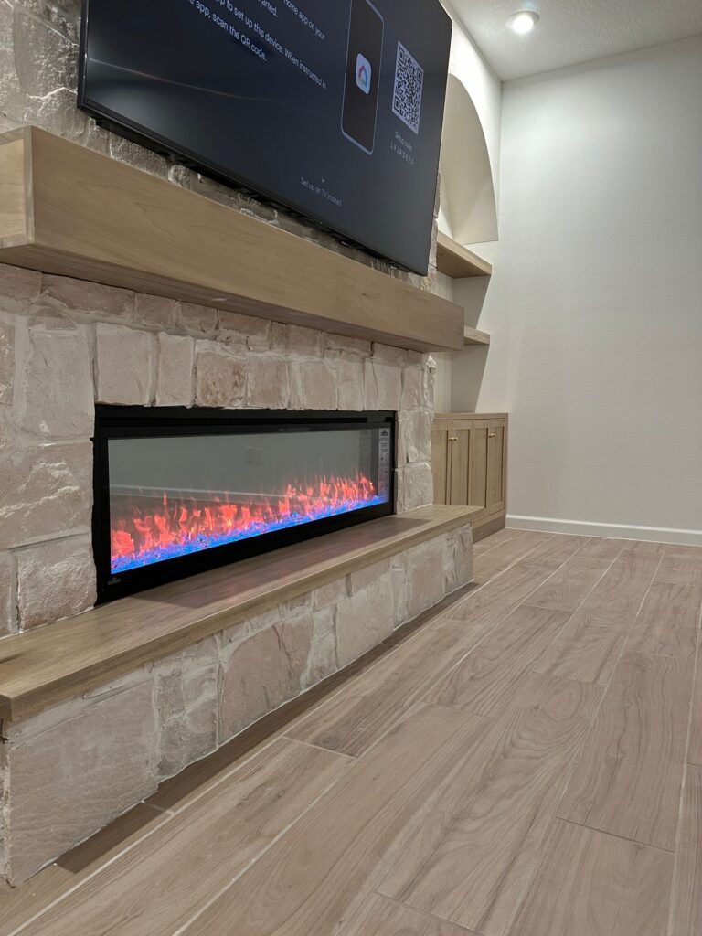 Rough cut stone fireplace wall with wood mantel, linear electric fireplace, and oversized textured stone surround