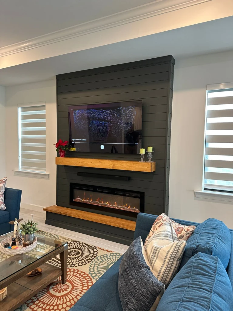 Angled view of the completed dark shiplap media wall with TV, fireplace, and wood accents