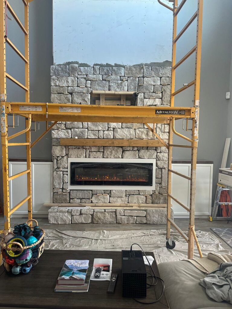 Limestone fireplace entertainment wall during stone installation with modern electric fireplace and full-height stone layout