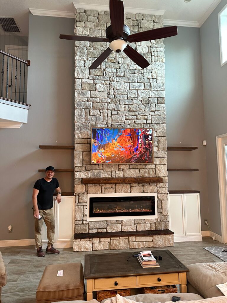 Finished 18-foot limestone fireplace entertainment wall with TV, electric fireplace, custom mantel, bench, and floating shelves