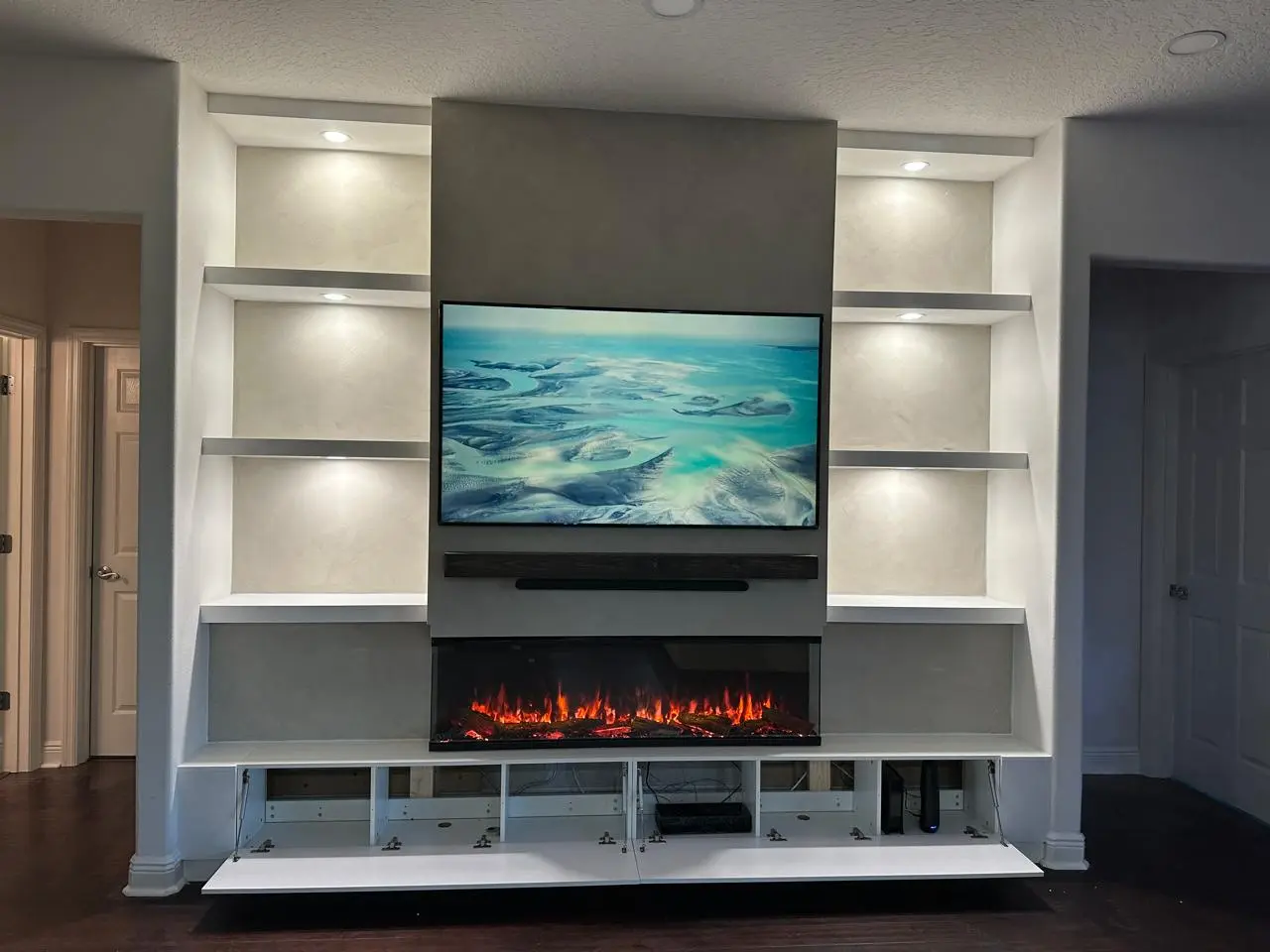 Limewash fireplace TV wall with built in shelving, hidden lower storage, integrated lighting, floating mantel, and 3D electric fireplace