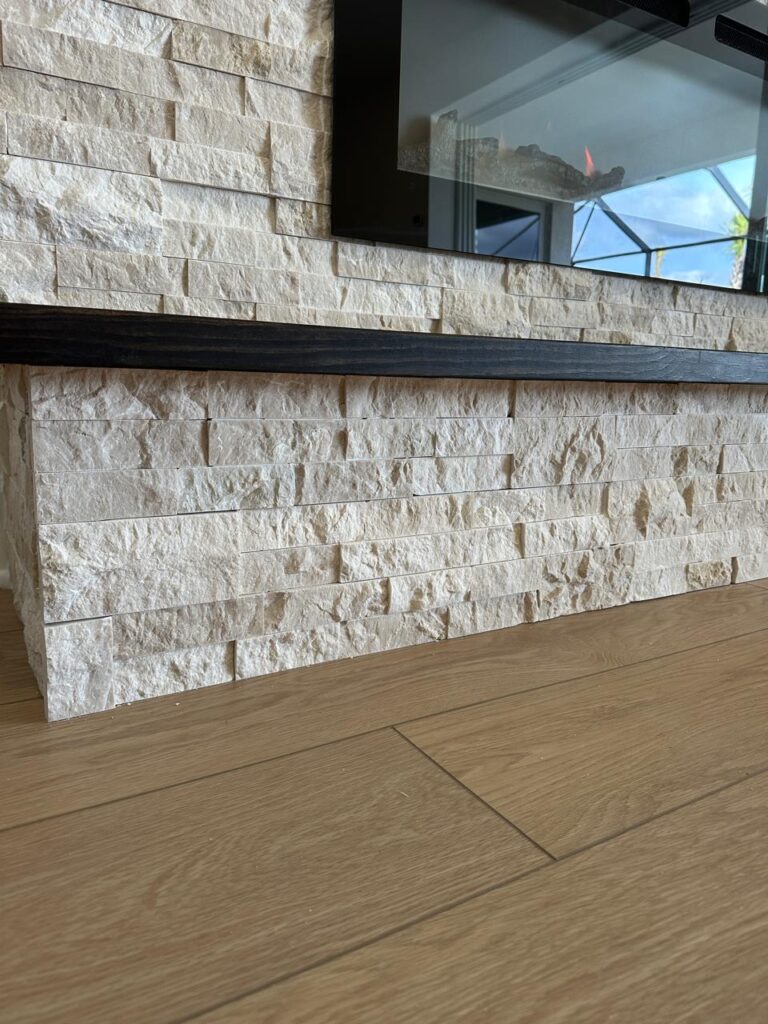 Stone fireplace media wall detail with mounted TV, floating wood mantel, and textured stone veneer