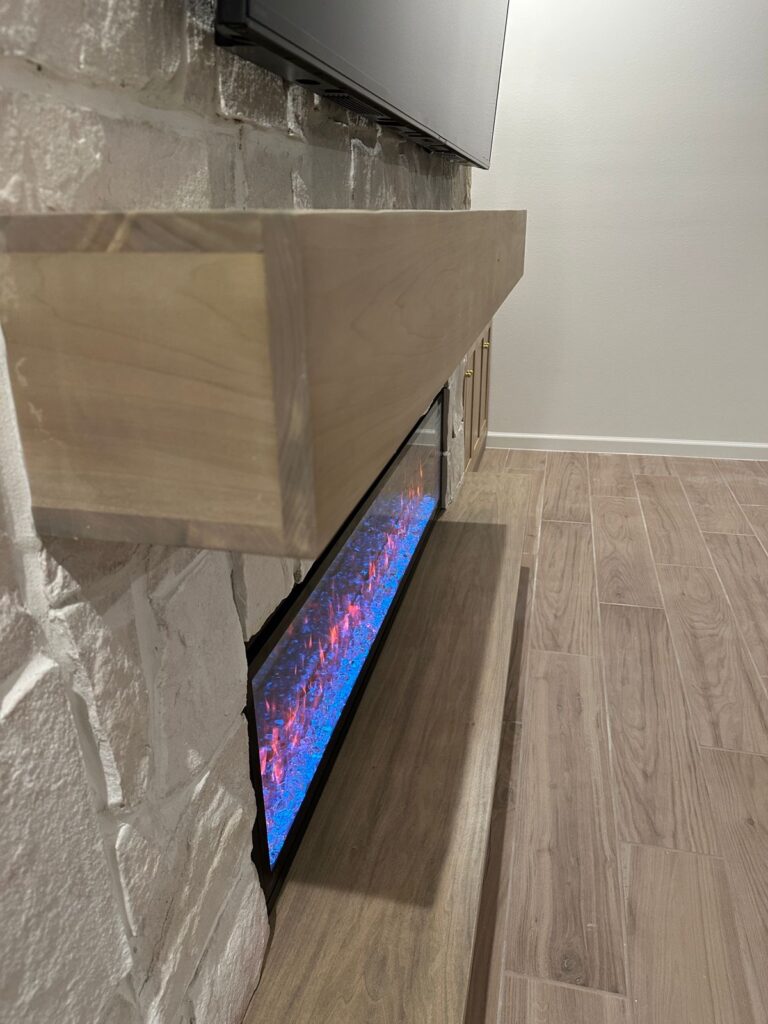 Finished rough cut stone fireplace wall with arched built-ins, floating wood shelves, cabinets, wood mantel, and linear fireplace