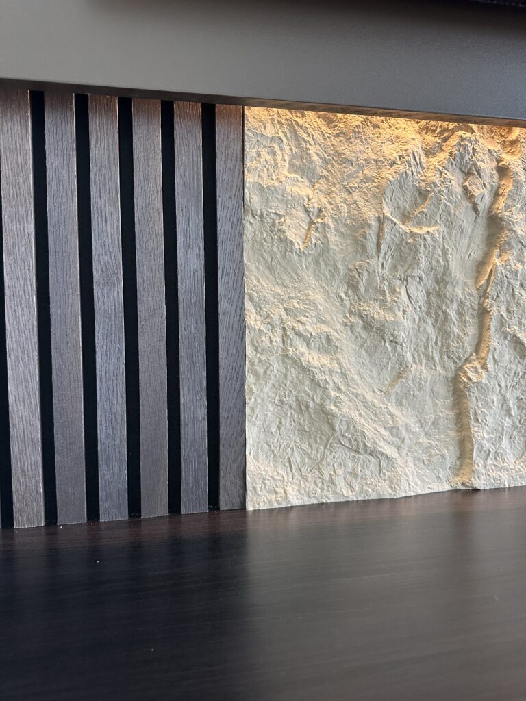 Close-up of acoustic panel media wall with black wood slats, textured wall finish, and warm LED accent lighting