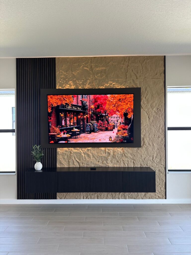 Finished acoustic panel media wall with recessed TV, black slat panels, textured stone-look finish, and floating cabinet