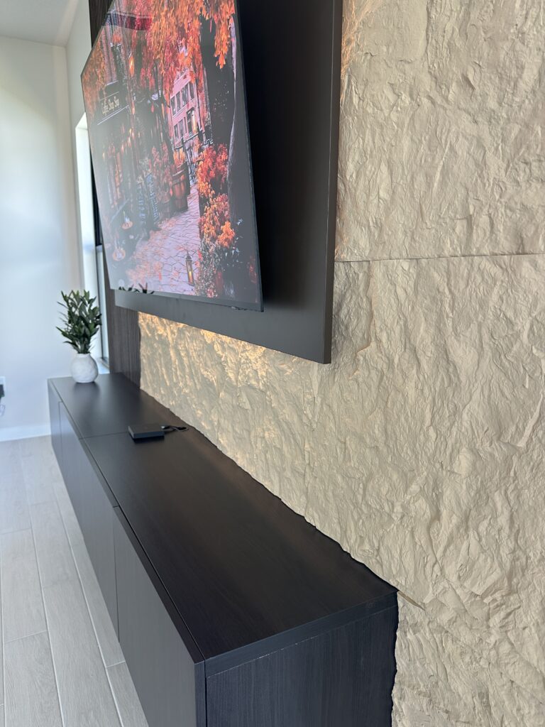 Side view of acoustic panel media wall with wall-mounted TV, textured stone-look finish, and floating black cabinet