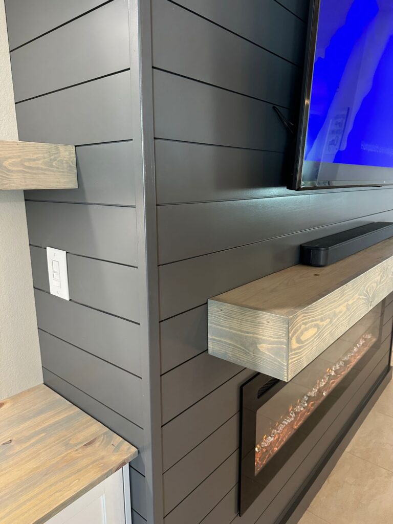 Close-up of a dark gray shiplap fireplace wall with floating wood mantel and linear electric fireplace