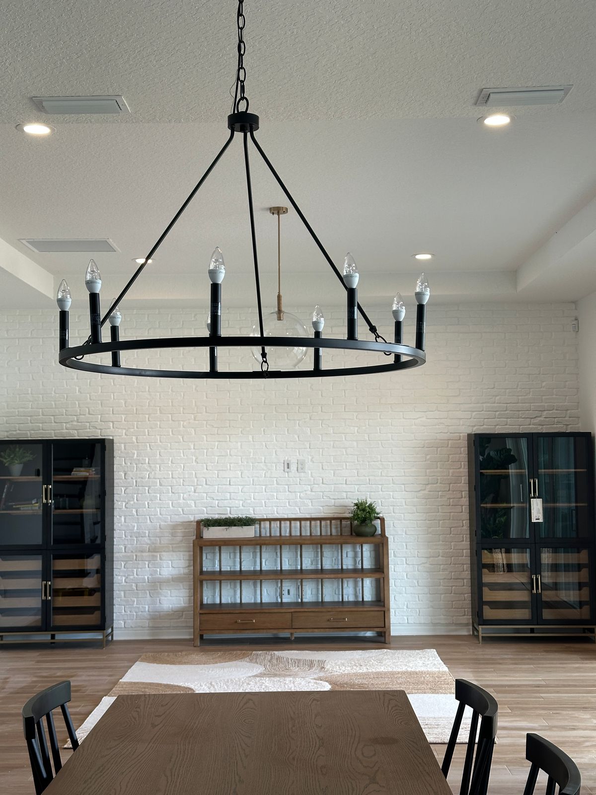 White brick accent wall with modern chandelier, black display cabinets, and warm dining room styling
