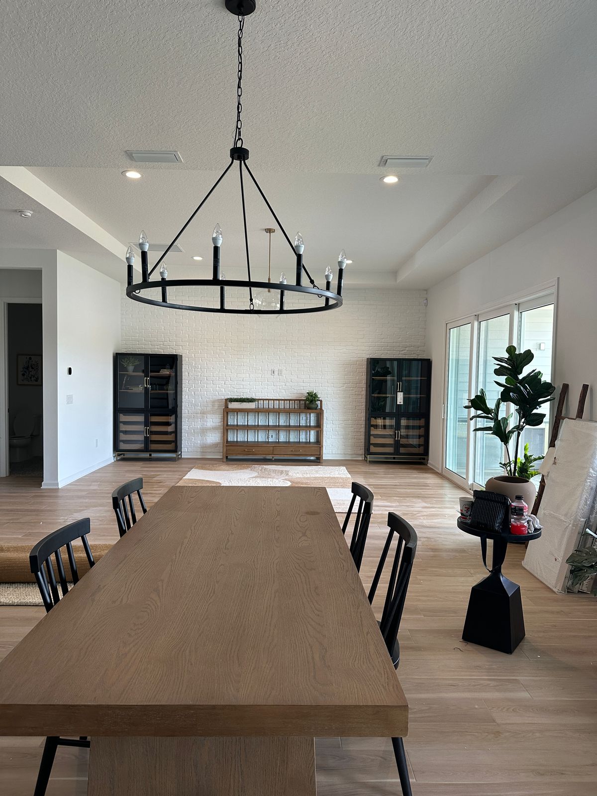 White brick accent wall in modern dining room with wood table, chandelier, and black display cabinets
