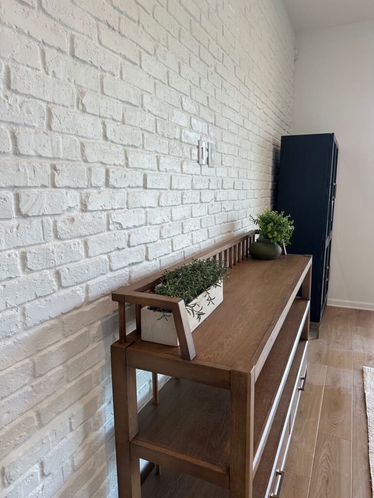 White brick accent wall with textured masonry finish, wood console, plants, and modern farmhouse styling