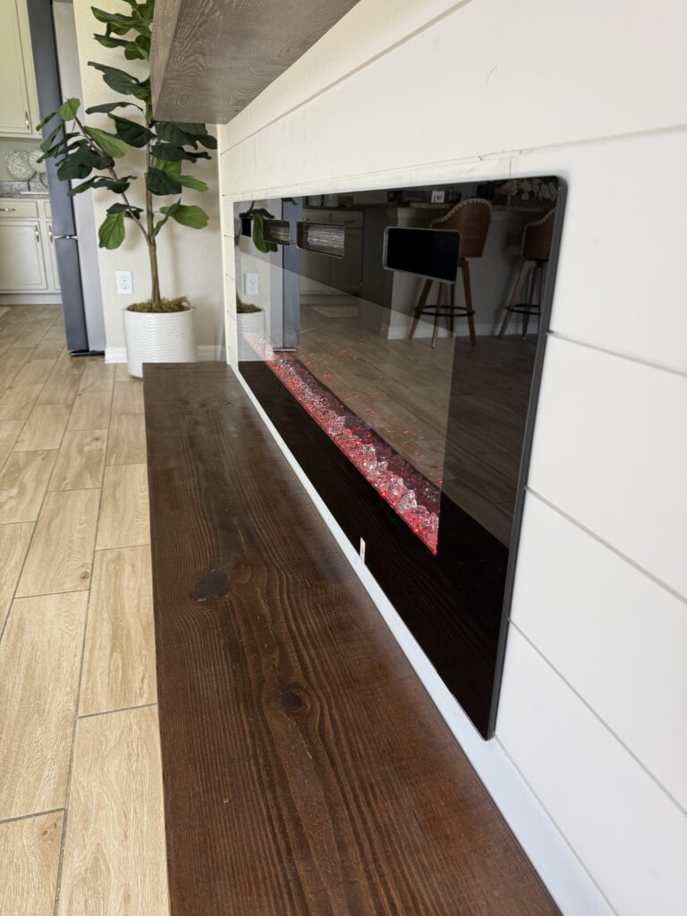 Close-up of the linear electric fireplace and stained wood bench on the white shiplap wall