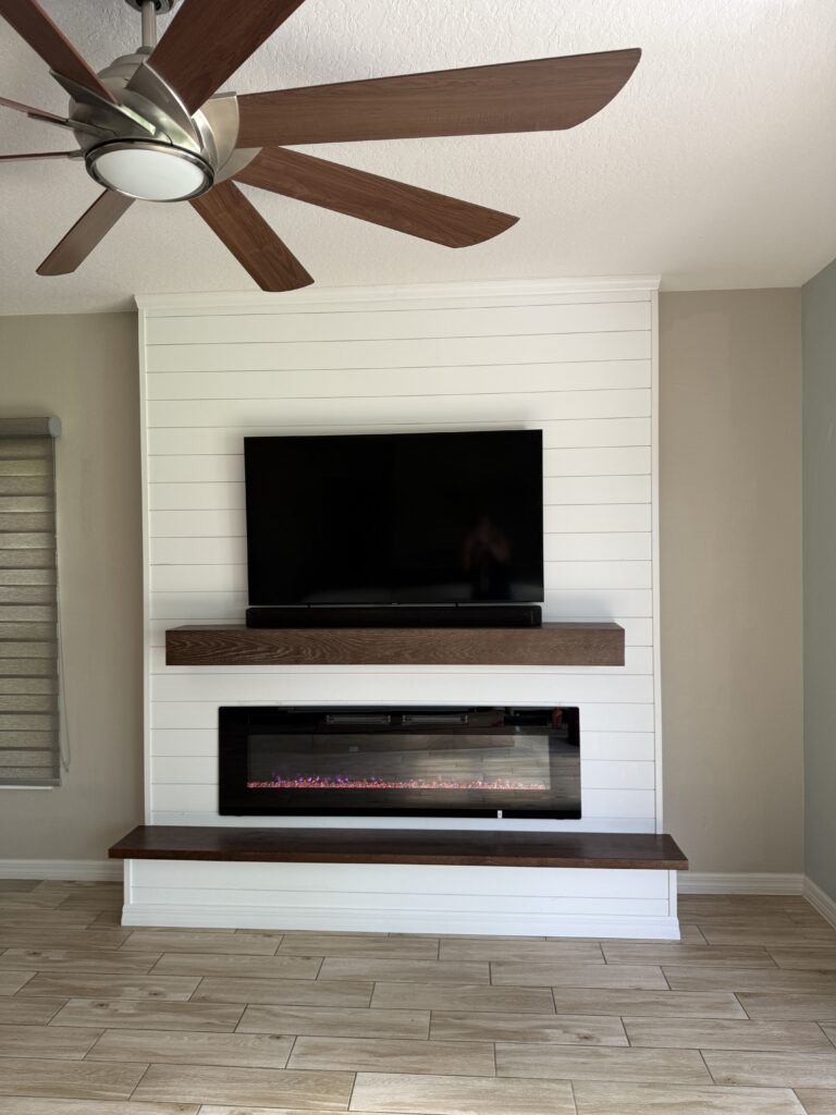 Front view of a white shiplap fireplace wall with TV, floating wood mantel, and matching bench