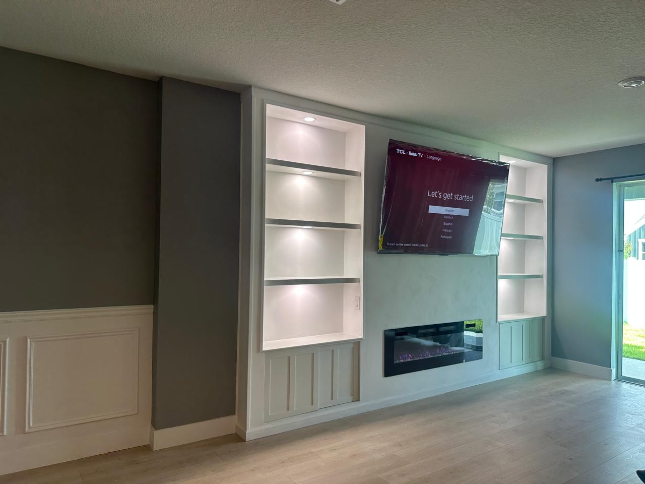 Built-in cabinetry in Palm Bay with illuminated shelves, sliding cabinet doors, limewash center wall, and electric fireplace