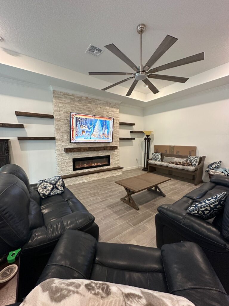 Floor-to-Ceiling Stone Fireplace Media Wall Floor-to-ceiling stone media wall with recessed TV, linear electric fireplace, floating wood shelves, and built-in cabinets