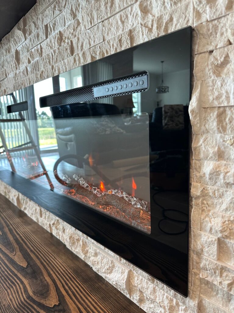 Linear Fireplace in Stone Media Wall Close-up of a linear electric fireplace installed in a textured stone media wall with a dark wood hearth bench