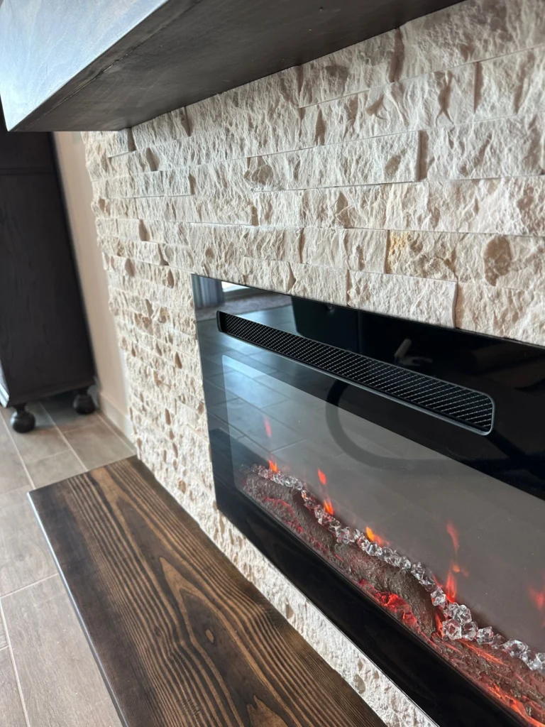 Stone Fireplace Wall Detail Textured stone fireplace wall with black linear electric insert and custom dark wood mantel