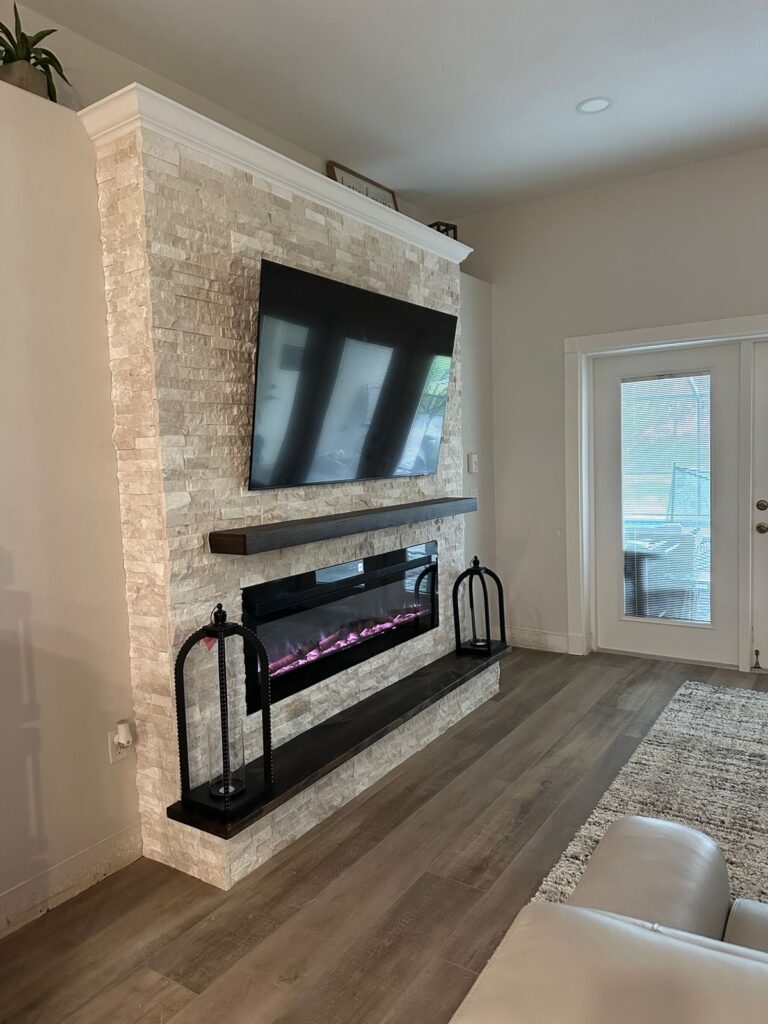 ledger-stone-fireplace-wall-in-melbourne-side-view.jpg Side view of a ledger stone fireplace wall in Melbourne with dark wood mantel, hearth bench, crown molding, and electric fireplace