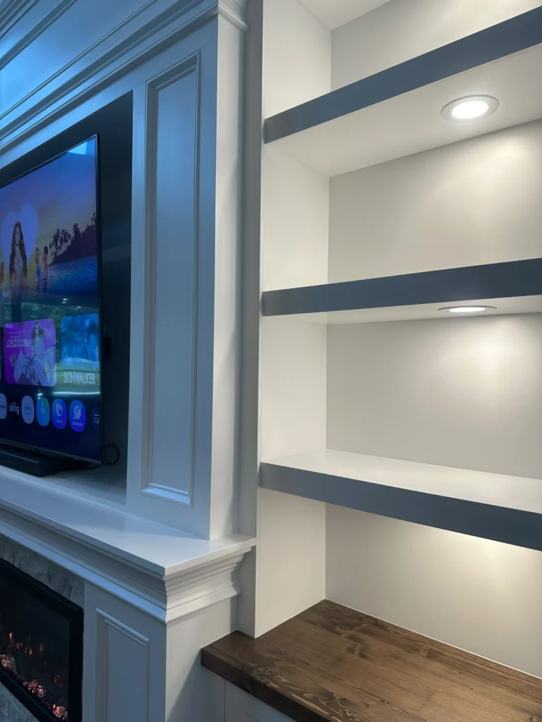 Recessed TV niche beside illuminated built-in display shelving