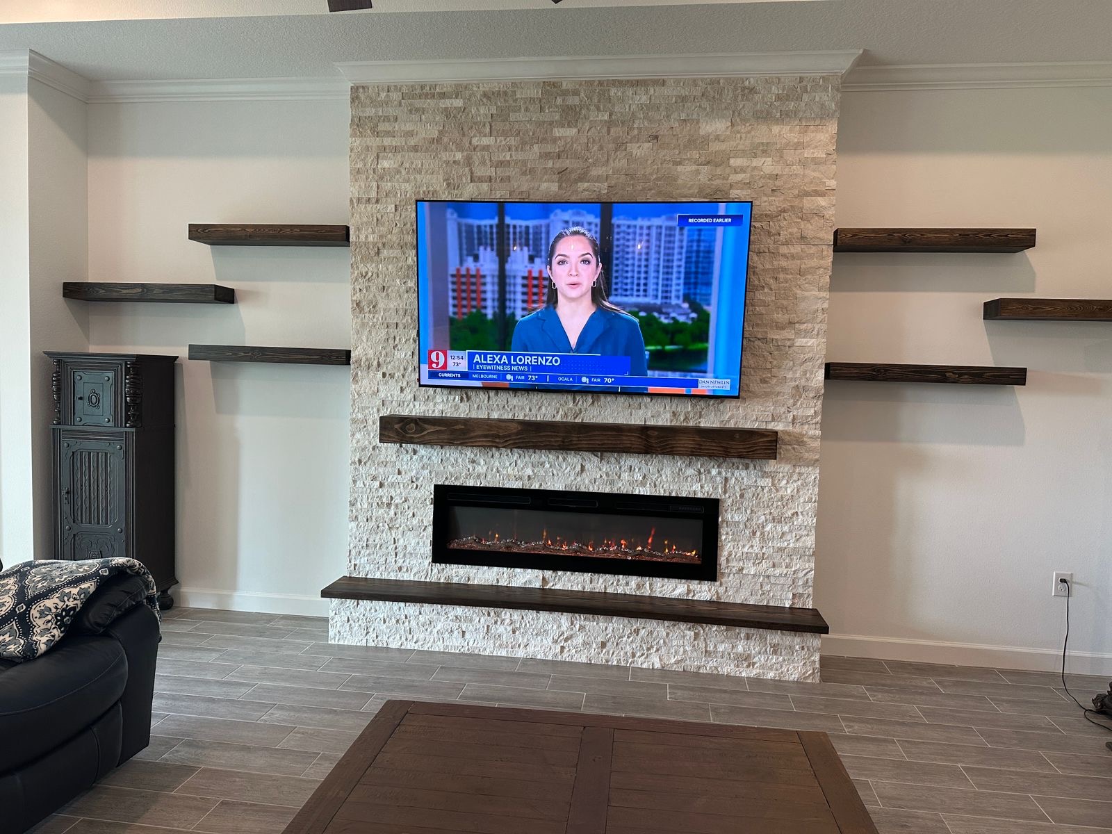 Stone fireplace media wall in Tampa with dark wood floating shelves, mounted TV, and linear electric fireplace