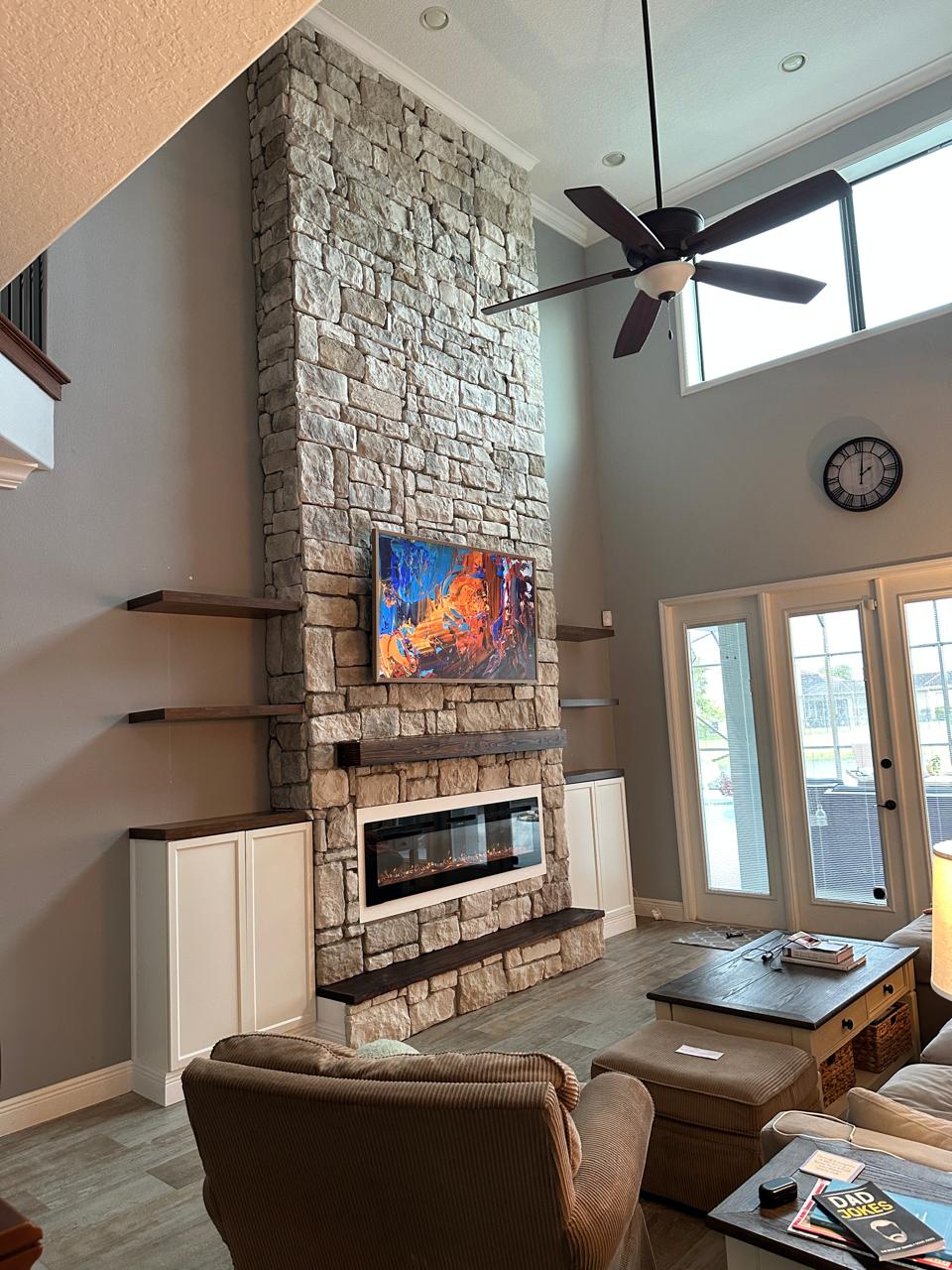 Stone media wall in Tampa with floor-to-ceiling stone, floating wood shelves, built-in cabinets, TV, and electric fireplace