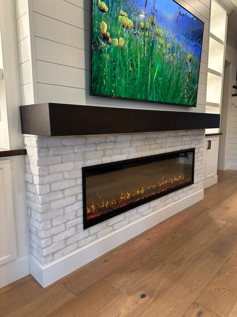 White brick fireplace wall with a handcrafted mantel and modern linear electric fireplace