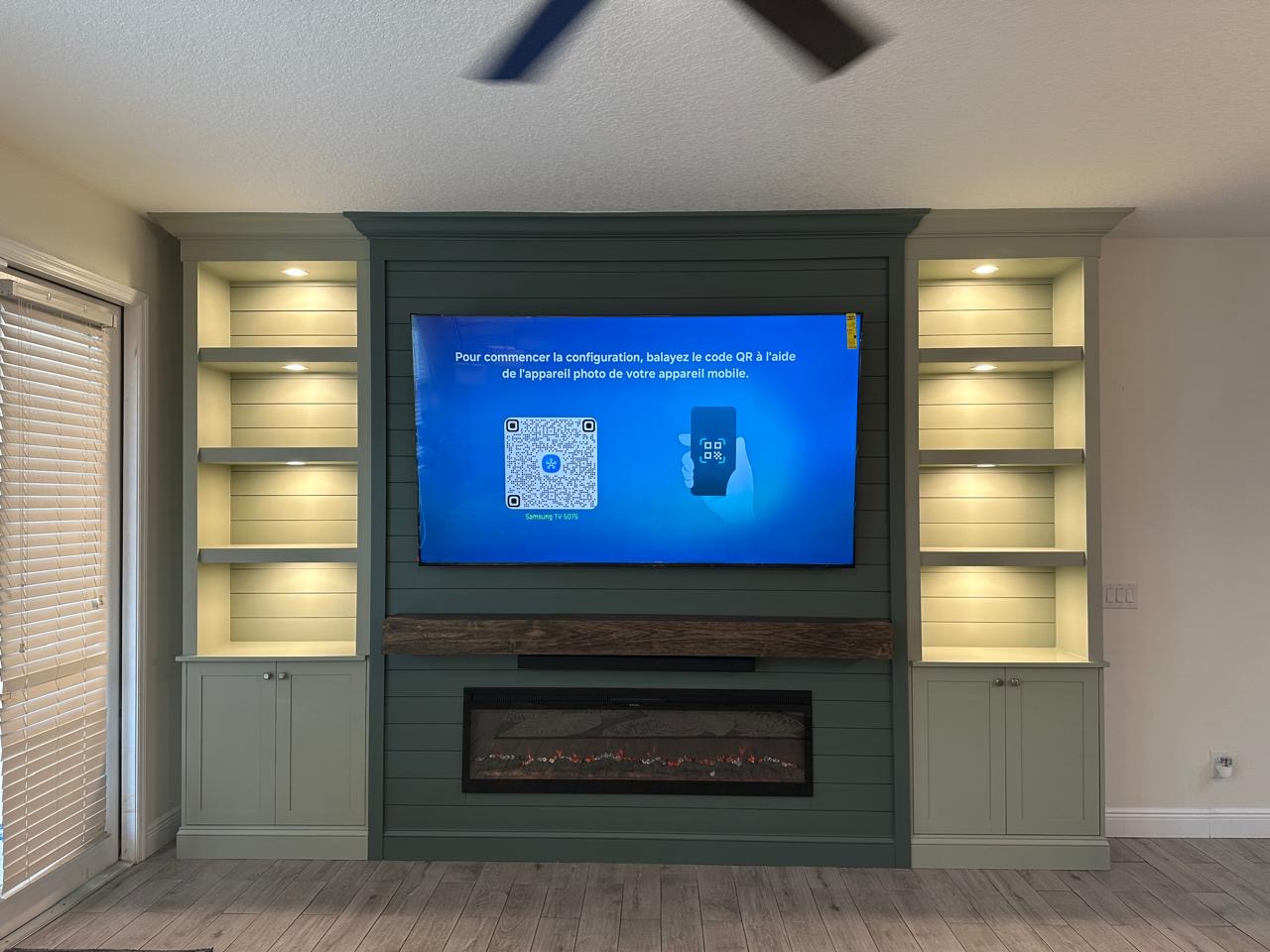 Completed Luxury TV Media Wall in Windermere Front view of the completed luxury TV media wall in Windermere with illuminated built-ins, sage green shiplap, wood mantel and electric fireplace