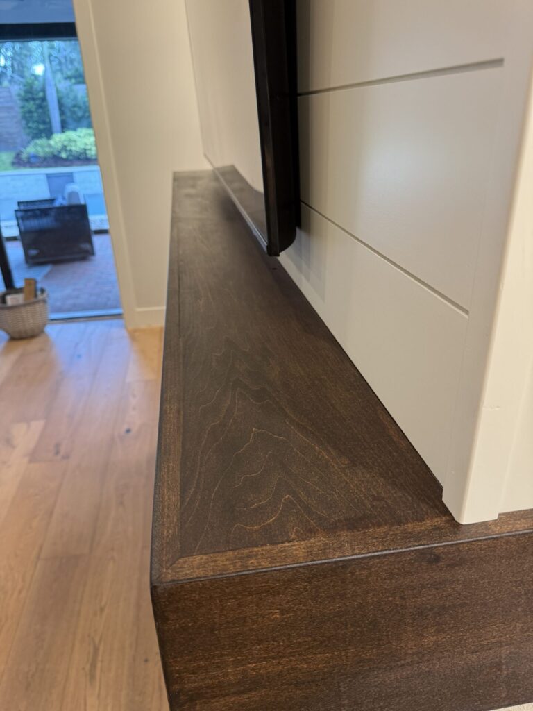 Handcrafted full-width dark wood mantel installed below the TV on a custom media wall
