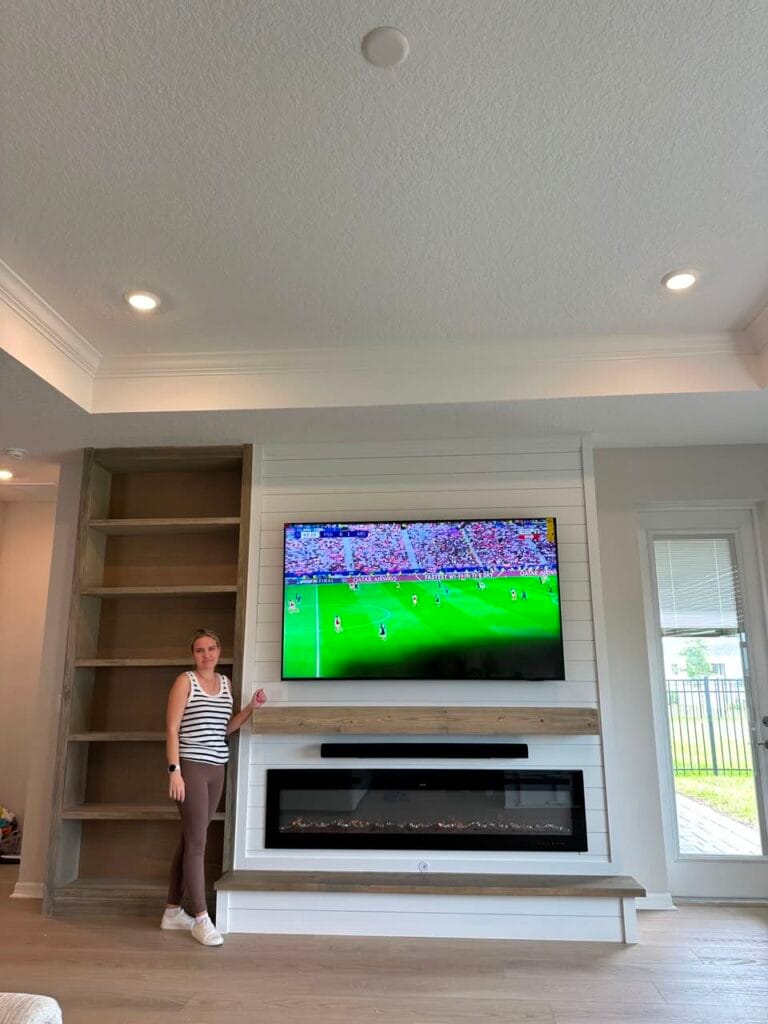 Completed white shiplap fireplace wall with wood mantel, storage bench, soundbar, and side shelving