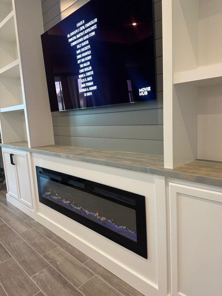 Electric Fireplace and Cabinetry Detail — Palm Bay Linear electric fireplace beneath a wood-toned countertop, with white cabinetry and gray shiplap behind the TV.