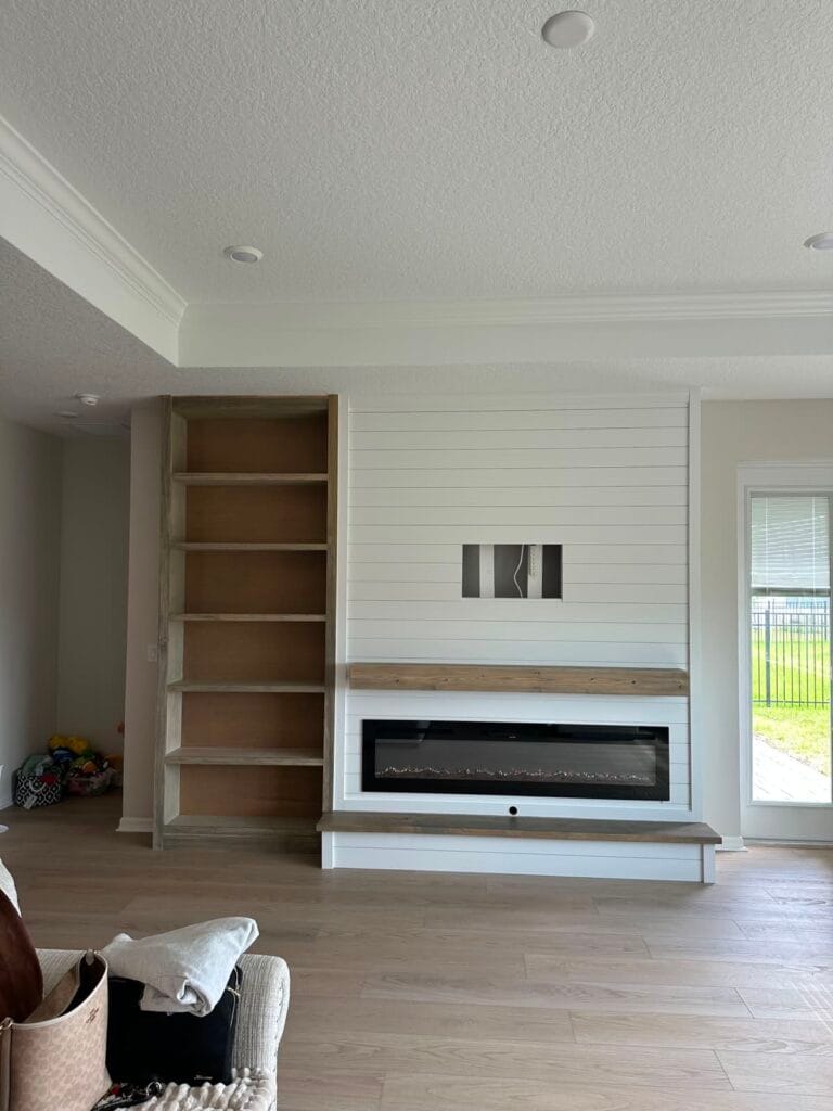 White shiplap fireplace wall during installation with wood bench and left-side shelving